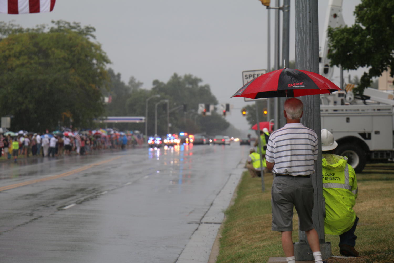 Community members shelter under umbrellas and hard hats as Sgt. Hunters procession nears.
