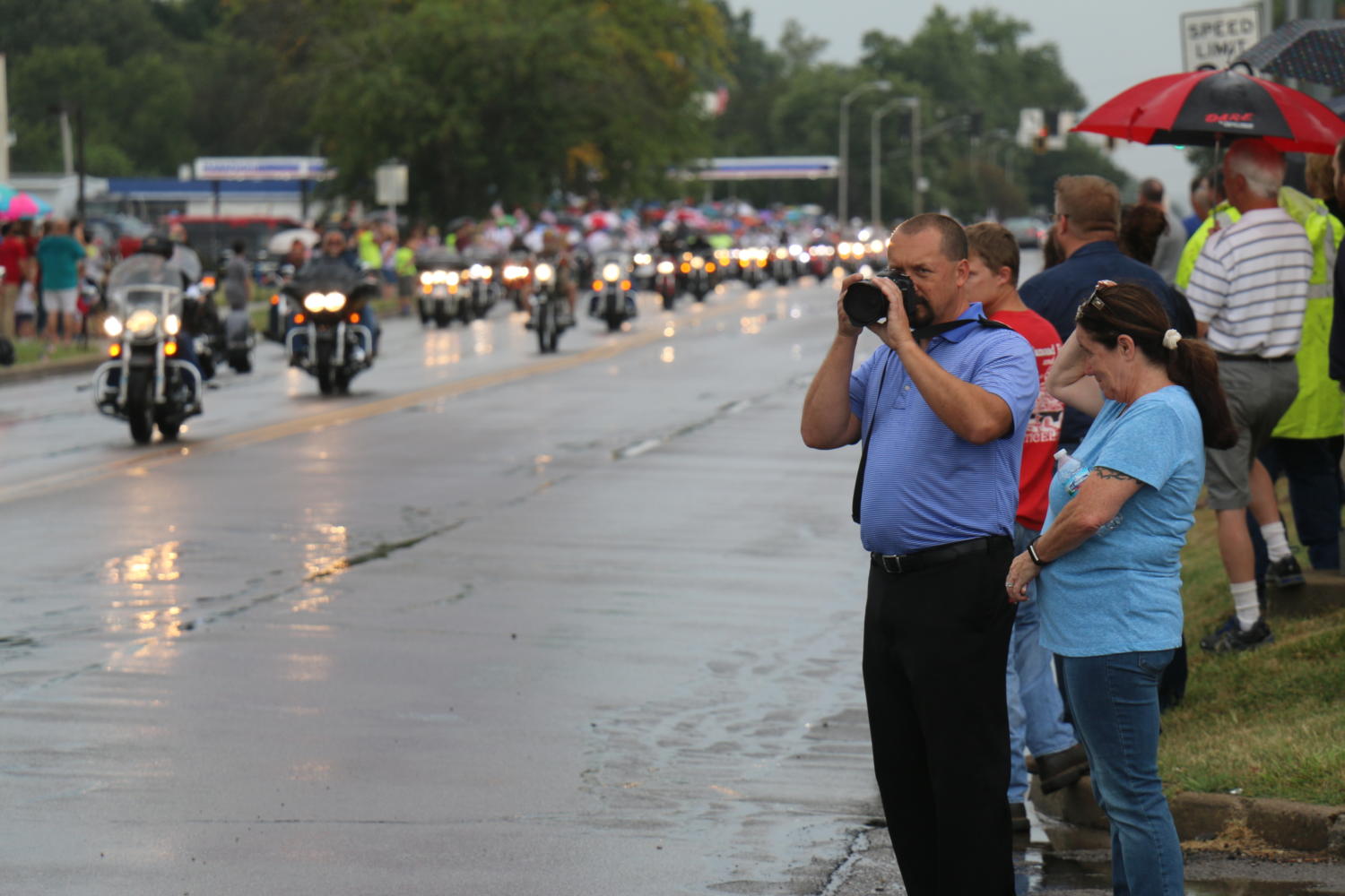 A community member pauses in photographing the procession as veteran motorcyclists pass. 