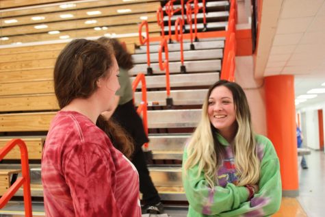 Two students chat while attendance is taken for gym class.